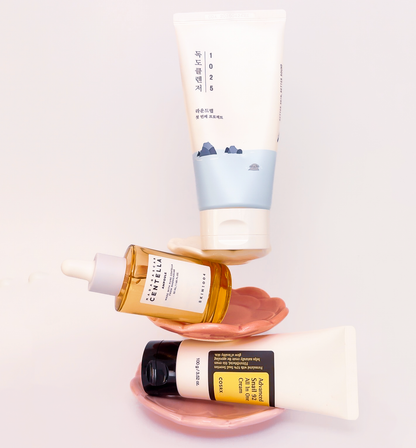 Koreanisches Hautpflege-Set auf rosa Keramikschalen: Round Lab 1025 Dokdo Cleanser, SKIN1004 Centella Ampoule und COSRX Snail 92 Creme