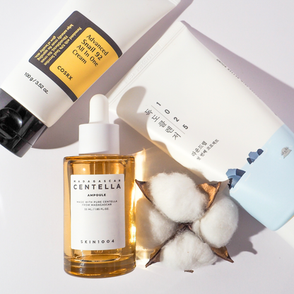 K-Beauty Flatlay mit COSRX Advanced Snail 92 All In One Cream, SKIN1004 Madagascar Centella Ampoule und Round Lab 1025 Dokdo Cleanser, dekoriert mit Baumwollkapseln